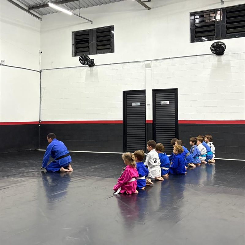 Turma infantil de judô ajoelhada no tatame diante do sensei